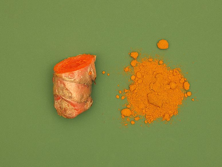 Bright Orange turmeric root and powder on a green background.