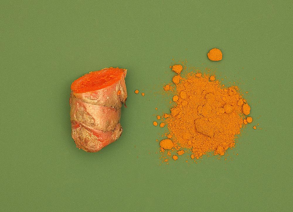 Bright Orange turmeric root and powder on a green background.