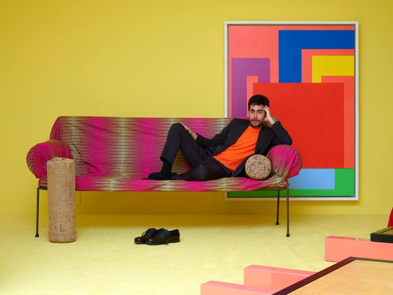 Omar Sosa reclining on a brightly colored couch in his brightly colored Friedman Benda show.