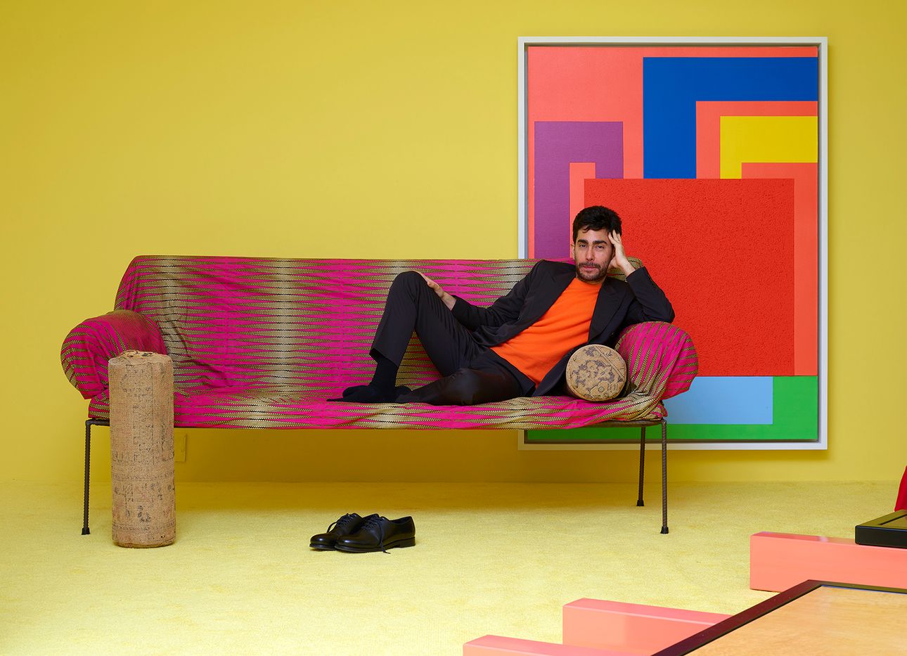 Omar Sosa reclining on a brightly colored couch in his brightly colored Friedman Benda show.