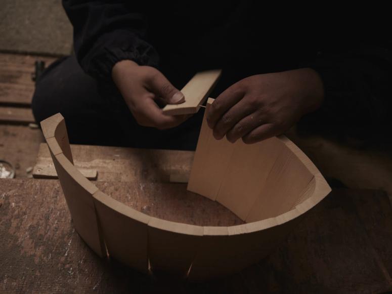 A man's hands assemble a wooden bucket on a wooden floor.