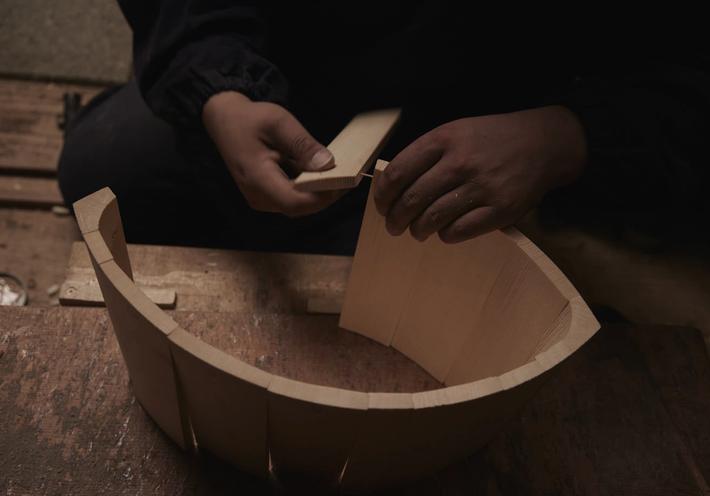 A man's hands assemble a wooden bucket on a wooden floor.