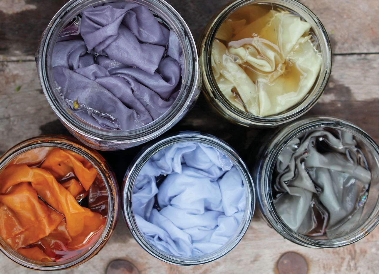Five dye pots with colored fabrics inside them.