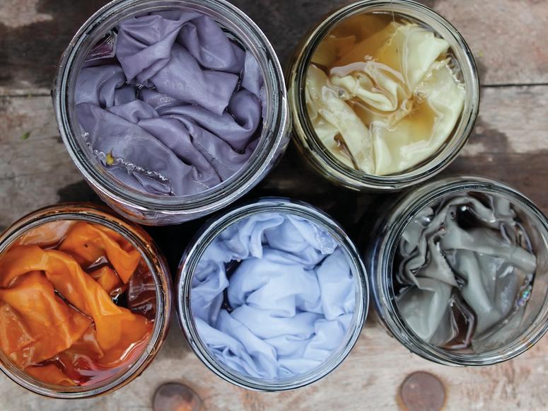 Five dye pots with colored fabrics inside them.