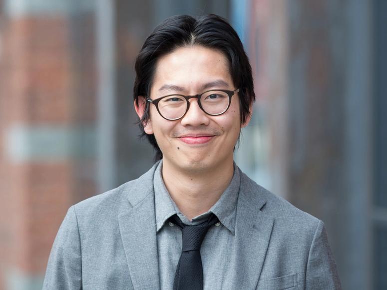 Nick Kwah in a grey suit, black tie, and glasses.
