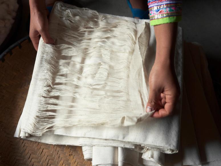 Hands holding the threads of a white roll of fabric.