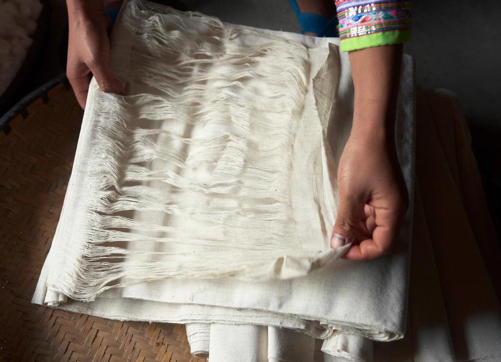Hands holding the threads of a white roll of fabric.