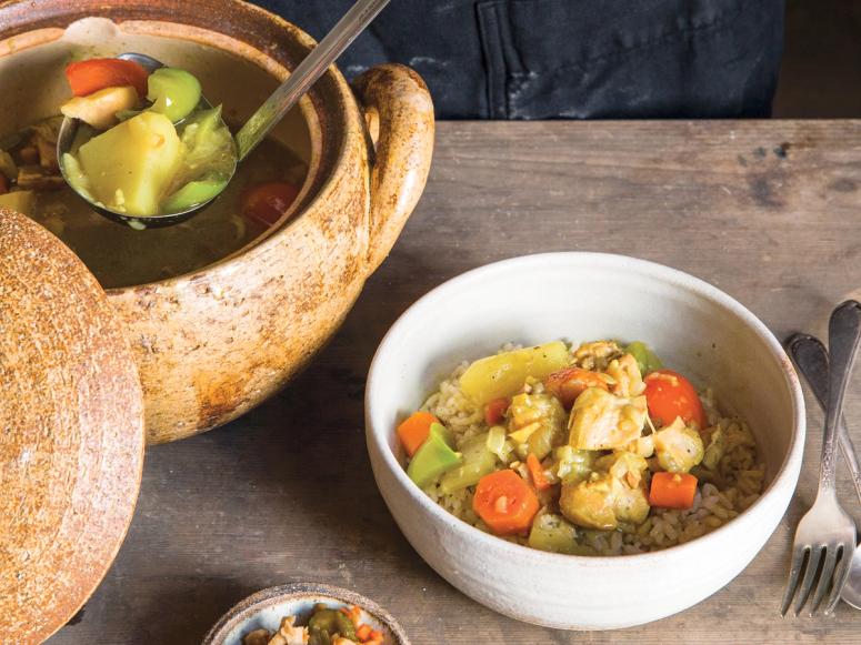 A ladle ladling Japanese chicken curry from a large clay pot into a bowl.