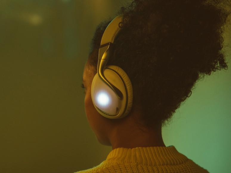 A woman with white headphones on a green background.