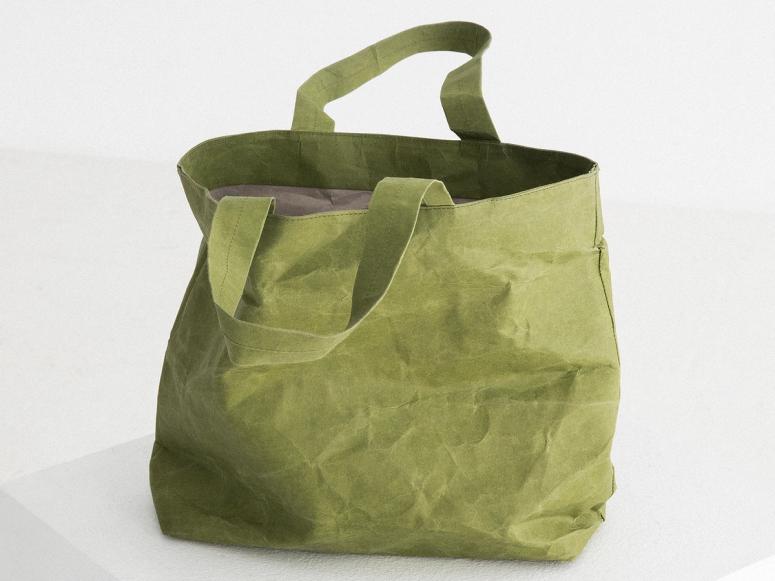 A crinkled green tote bag on a white plinth.