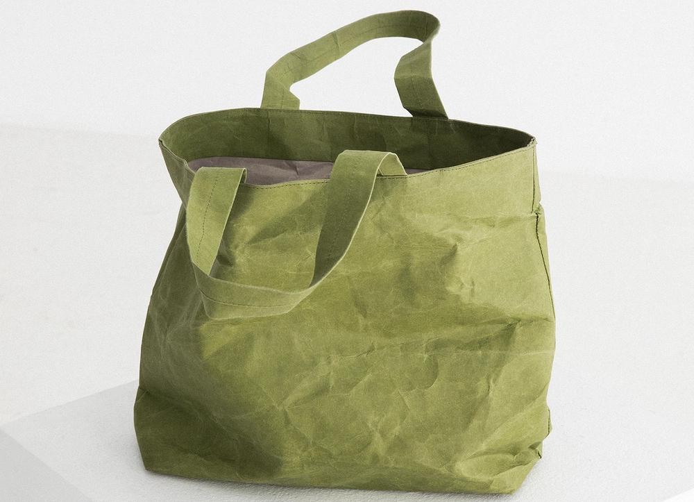 A crinkled green tote bag on a white plinth.