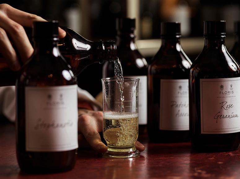 A hand pouring a bottle of fragrance into a beaker.