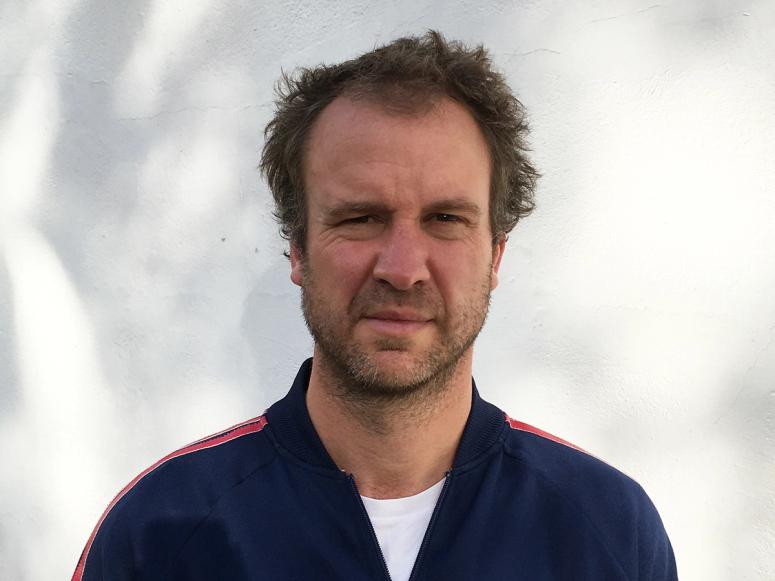 Malcolm James in a blue tracksuit, in front of a white background.