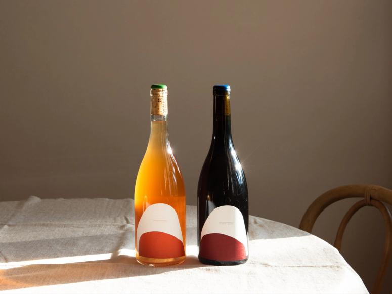 Orange and red bottles of wine in the sunlight on a natural linen tablecloth.