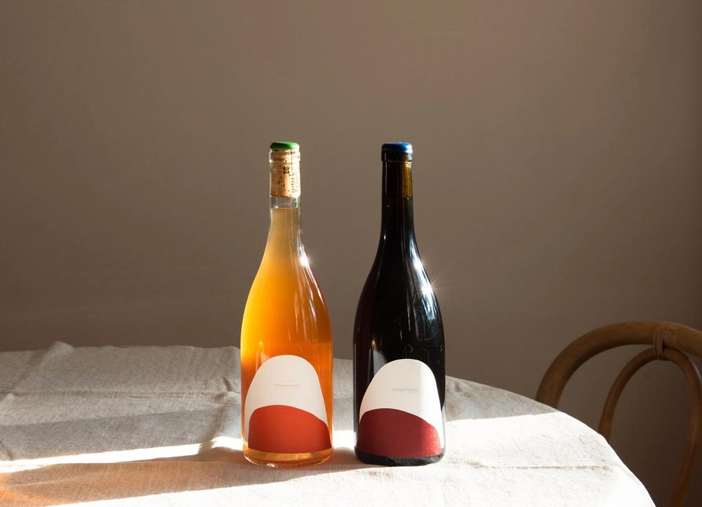 Orange and red bottles of wine in the sunlight on a natural linen tablecloth.