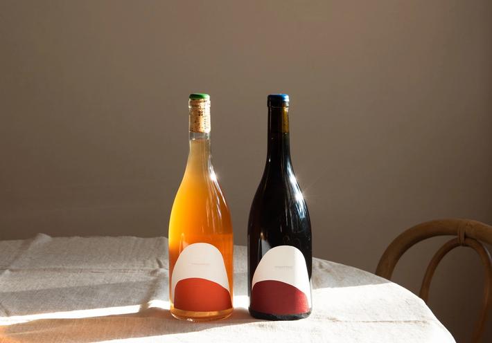 Orange and red bottles of wine in the sunlight on a natural linen tablecloth.