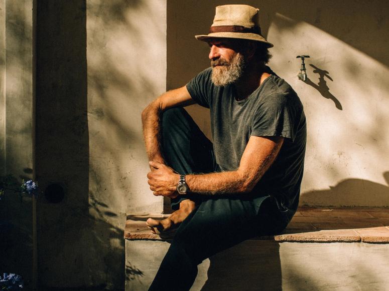 A man sitting outside barefoot wearing a hat