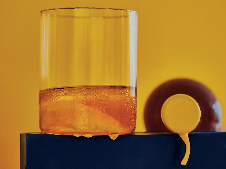 A dark orange glass of génépy on a yellow background.