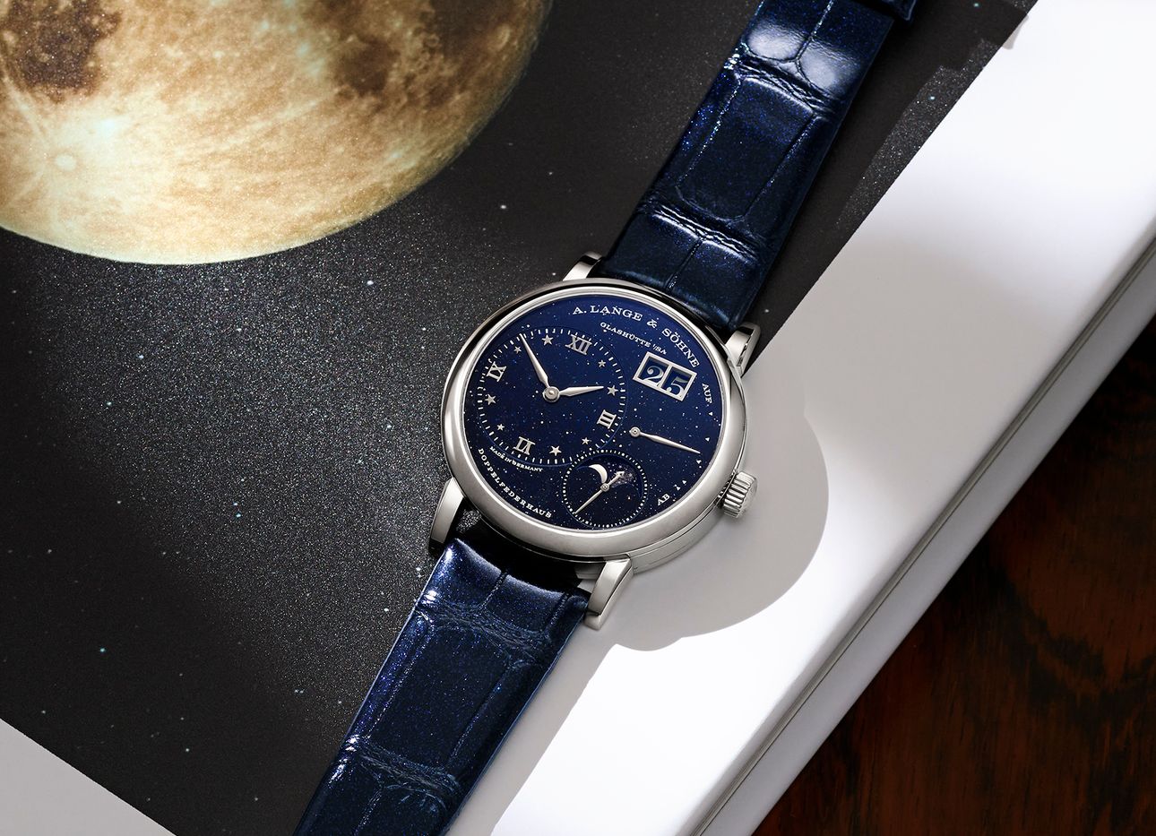 A navy blue watch on a desk next to a picture of the moon