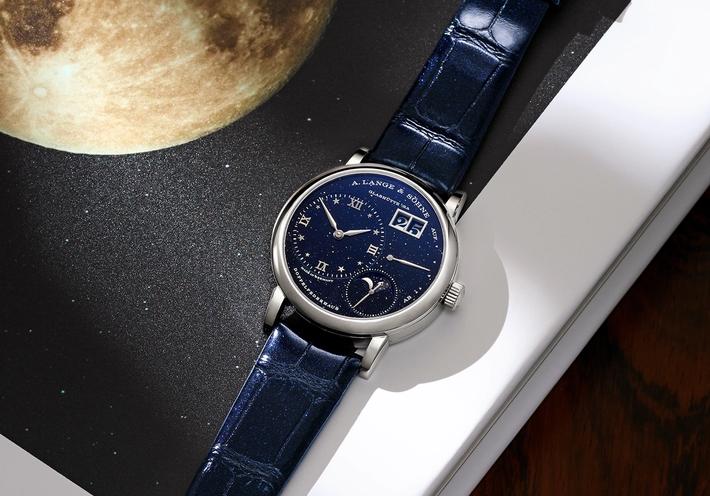 A navy blue watch on a desk next to a picture of the moon