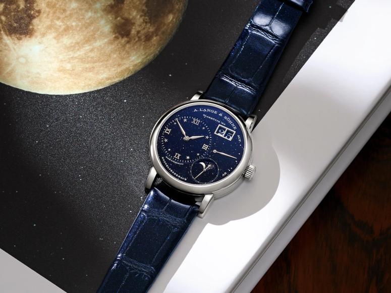 A navy blue watch on a desk next to a picture of the moon