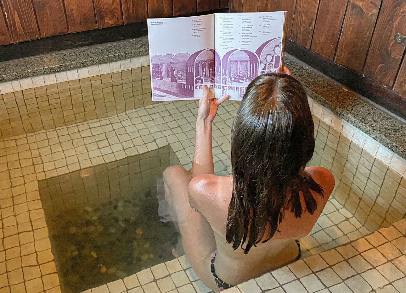A woman reads a magazine in a hot tub wearing a swimsuit