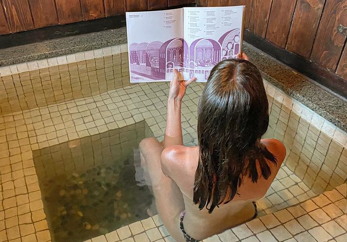 A woman reads a magazine in a hot tub wearing a swimsuit