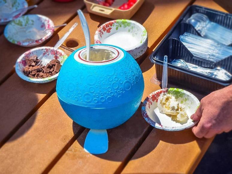 A ball used to make ice cream sitting on a picnic table