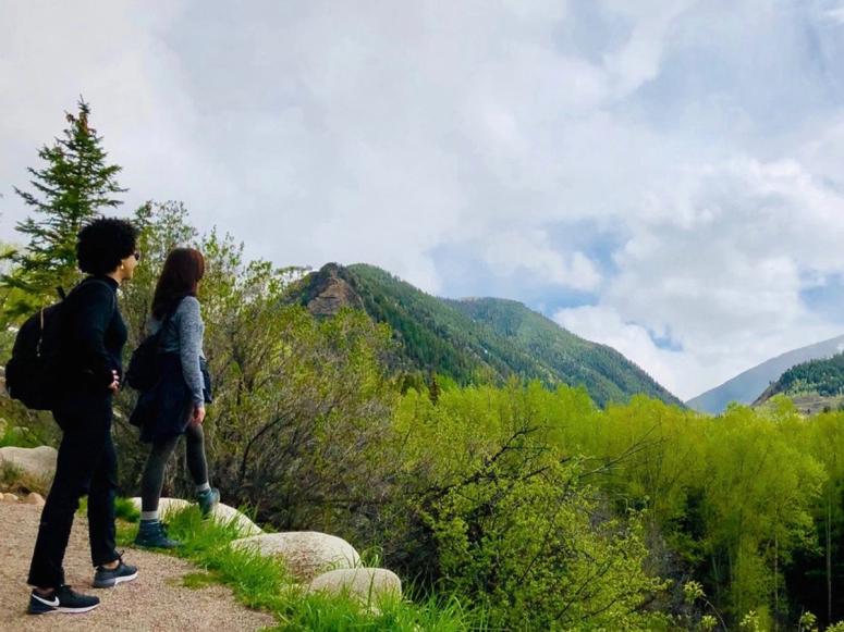 Dr. Ayana Elizabeth Johnson and Dr. Katharine K. Wilkinson looking out over green mountains from a patch of trail.