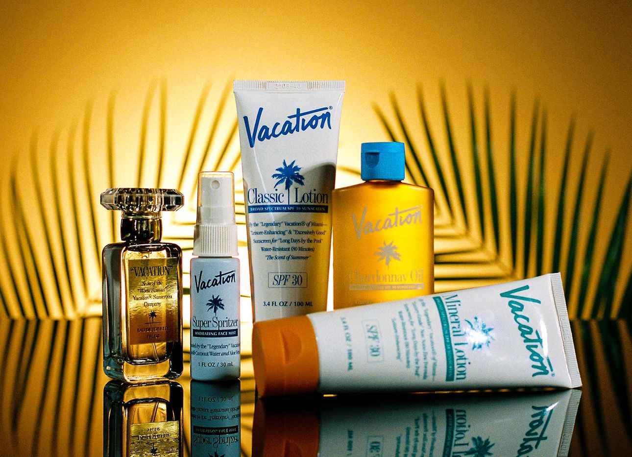 Tubes of sunscreen and a perfume shot in front of palm leaf branches