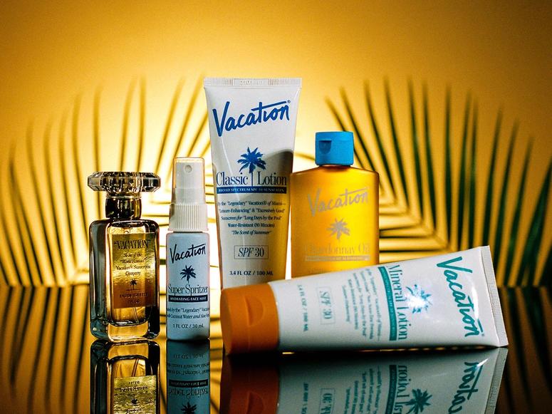 Tubes of sunscreen and a perfume shot in front of palm leaf branches