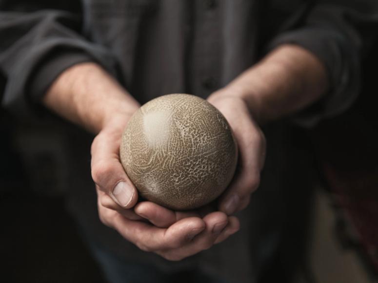 Two hands cupping a dorodango mud ball.