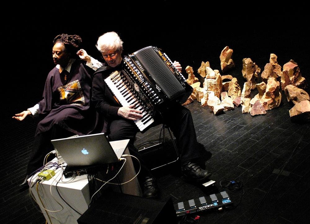 Pauline Oliveros and IONE performing on a black stage.