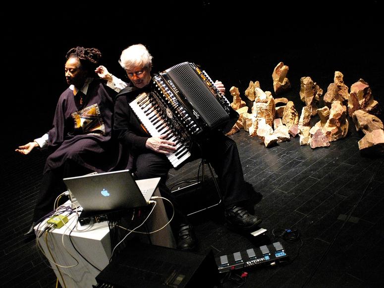 Pauline Oliveros and IONE performing on a black stage.