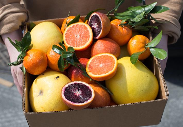 A box of orange, red, and yellow citrus fruits.