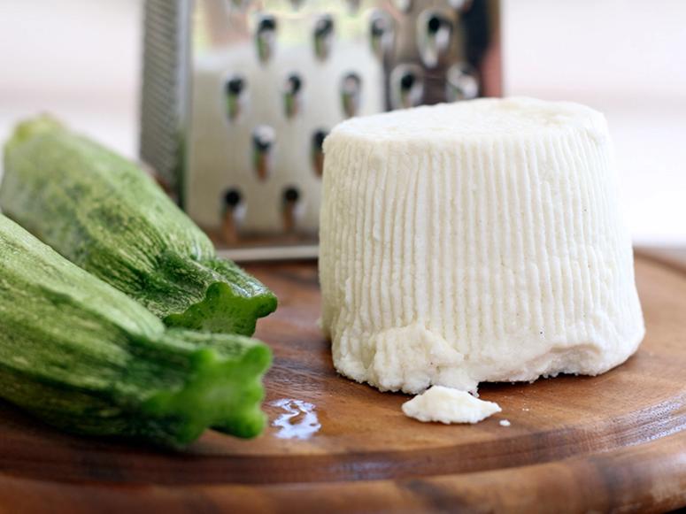 Ricotta on a carving board with a cheese grater and two pieces of okra.