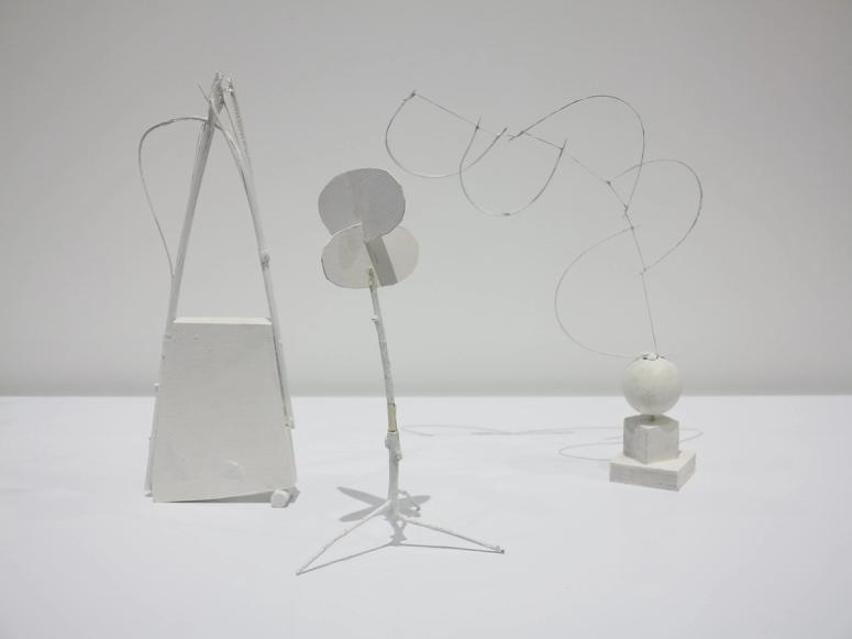 Three white, off-kilter sculptures on a white background.