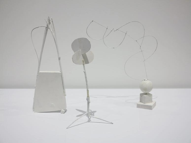 Three white, off-kilter sculptures on a white background.