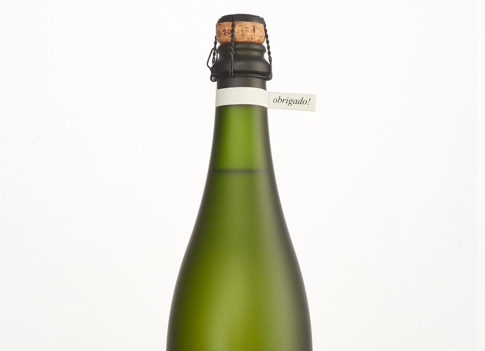 A green bottle of brut with a small tag around its neck reading "obrigado!"