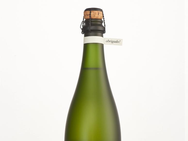 A green bottle of brut with a small tag around its neck reading "obrigado!"