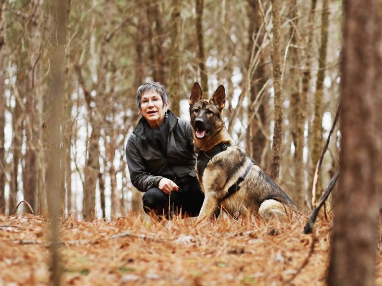 Author Cat Warren and one of her dogs, Rev, crouching in an autumn forest.