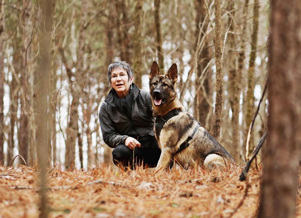Author Cat Warren and one of her dogs, Rev, crouching in an autumn forest.