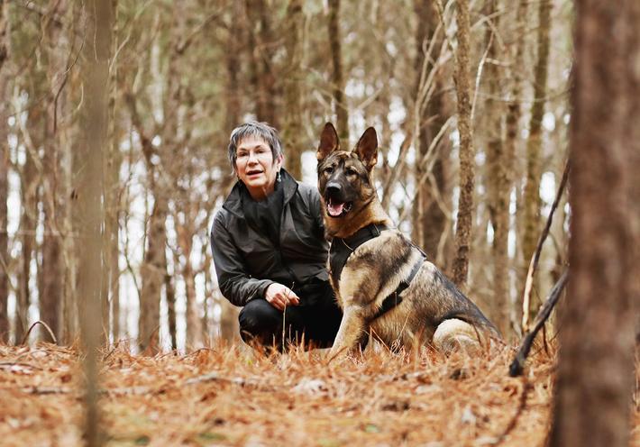 Author Cat Warren and one of her dogs, Rev, crouching in an autumn forest.