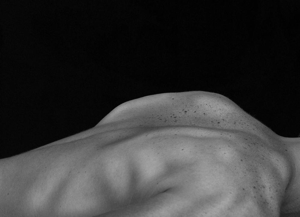 A person's bare back against a black background.