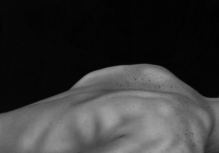 A person's bare back against a black background.