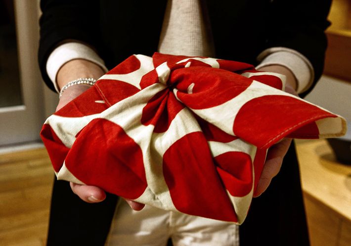 Someone presenting a gift wrapped in a red polka-dot tenegui.