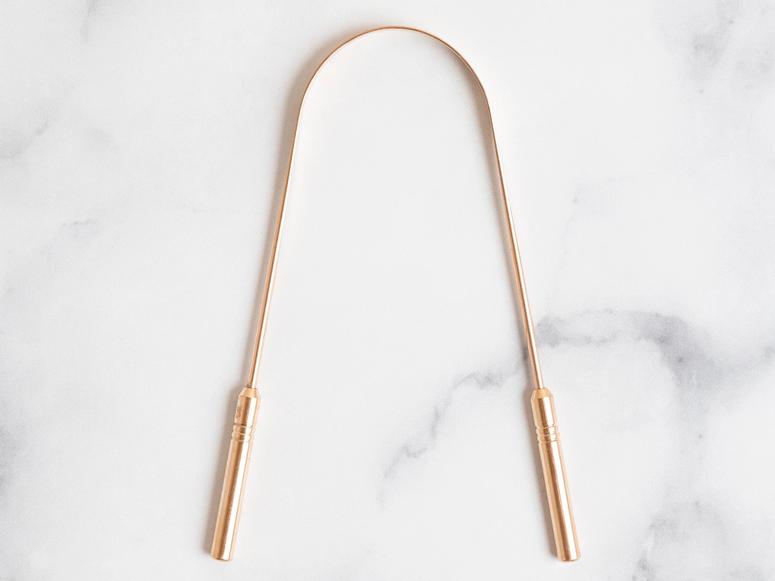 A gold tongue scraper on a white marble surface.