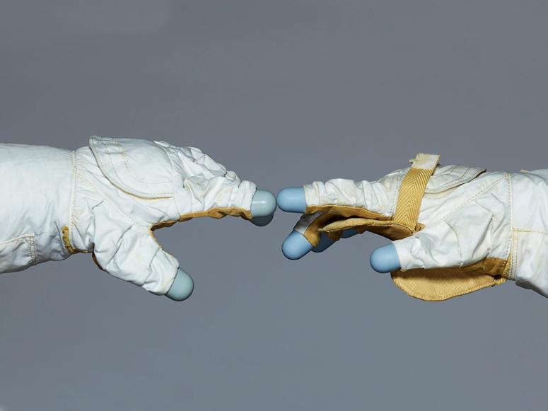 Two astronaut gloves touching on a grey background.