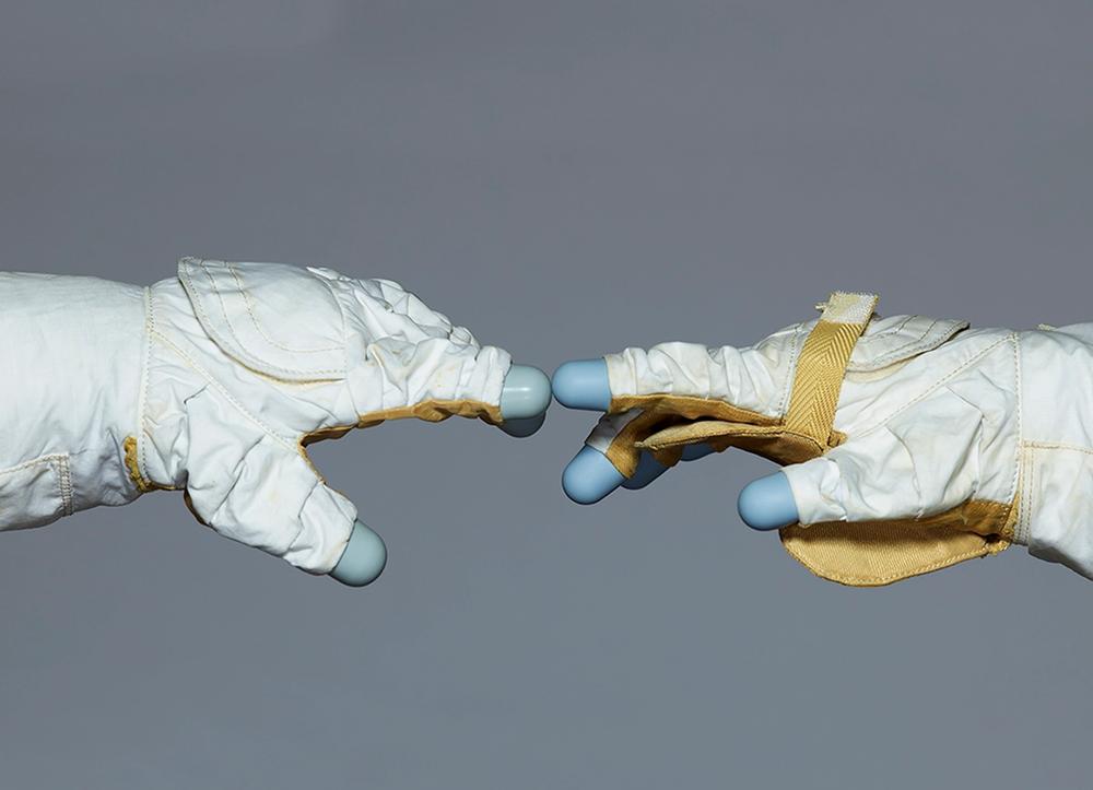 Two astronaut gloves touching on a grey background.
