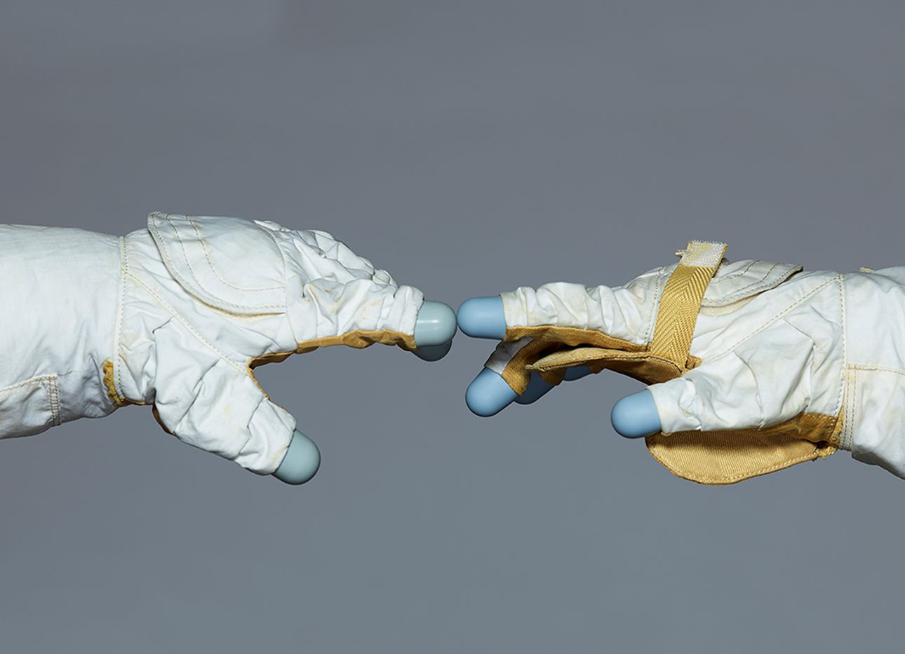 Two astronaut gloves touching on a grey background.
